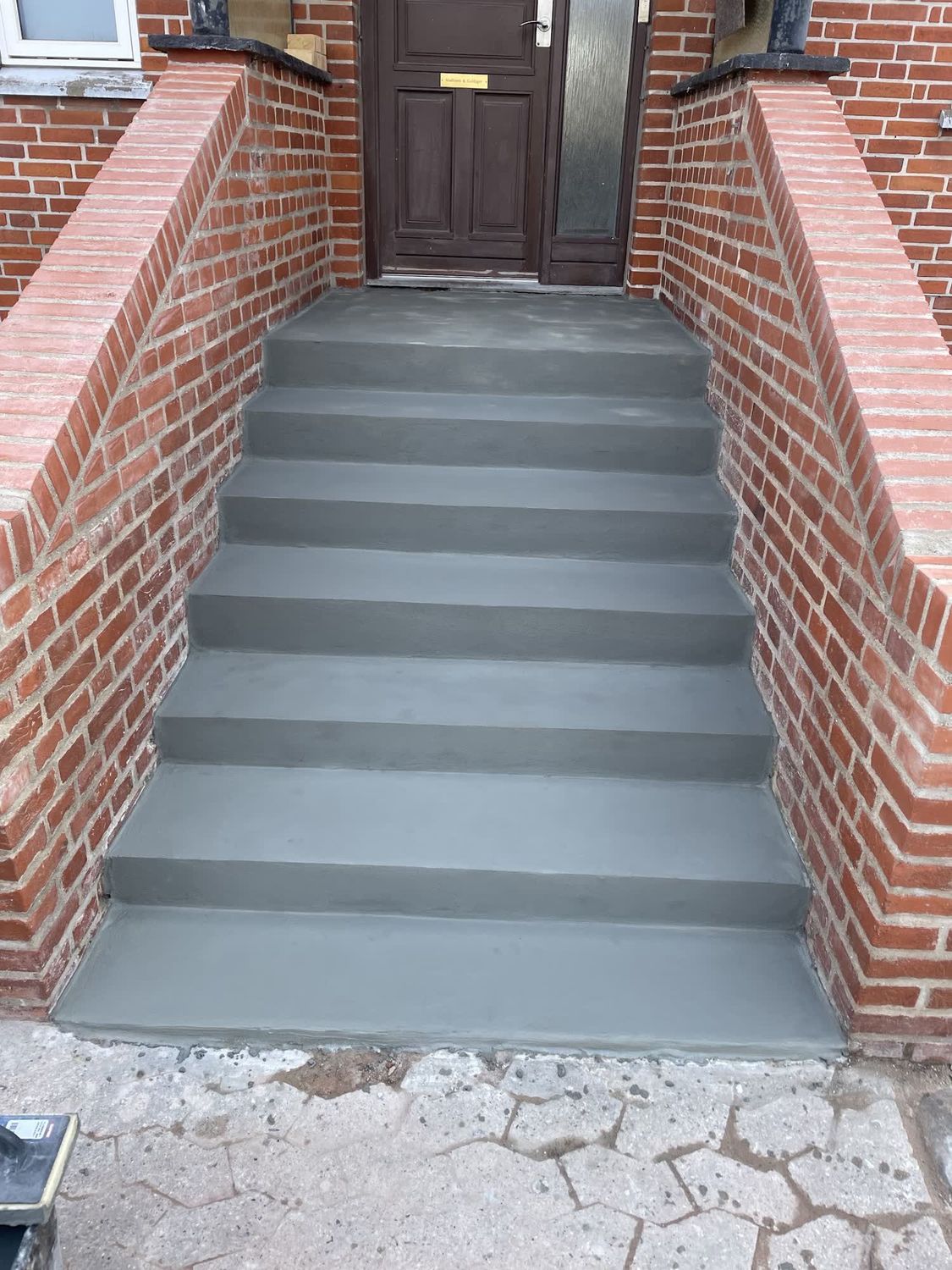 Betontrappe med grå fliser op til en hoveddør mellem to murede vanger